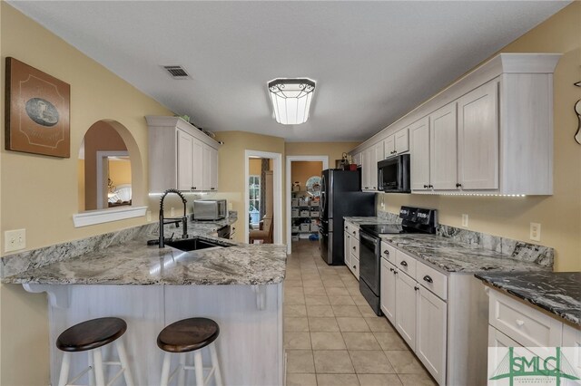 kitchen with kitchen peninsula, sink, black appliances, white cabinetry, and a breakfast bar area