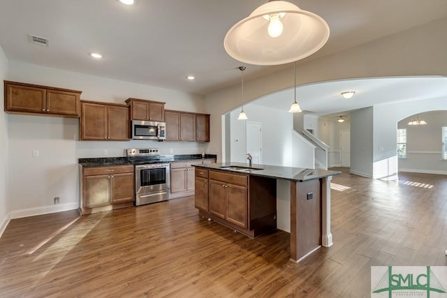 kitchen with stainless steel appliances, dark wood-type flooring, sink, a center island with sink, and hanging light fixtures