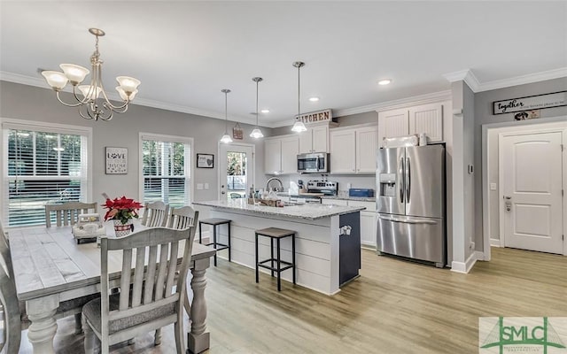 kitchen with white cabinets, hanging light fixtures, light hardwood / wood-style flooring, appliances with stainless steel finishes, and light stone counters