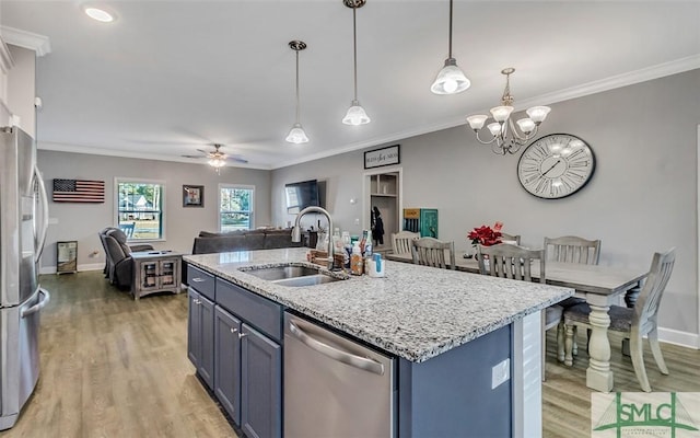 kitchen featuring appliances with stainless steel finishes, ceiling fan with notable chandelier, sink, hanging light fixtures, and an island with sink