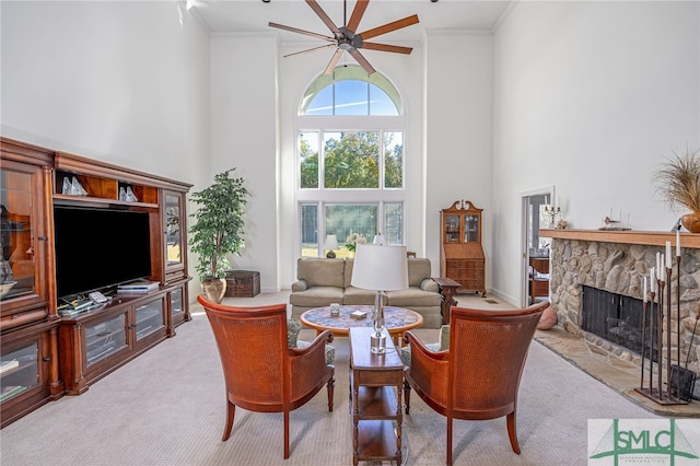 carpeted living room with ceiling fan, a fireplace, a high ceiling, and ornamental molding