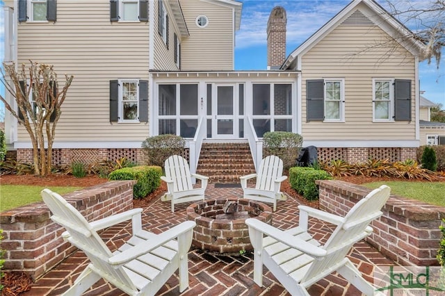 back of property with an outdoor fire pit, a patio area, and a sunroom