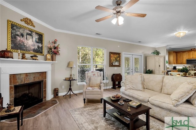 living room featuring ceiling fan, light wood-type flooring, crown molding, and a tile fireplace