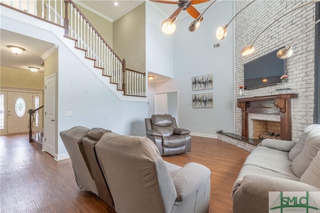 living room featuring a towering ceiling, ornamental molding, ceiling fan, wood-type flooring, and a fireplace