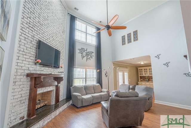 living room with ceiling fan, ornamental molding, a high ceiling, and light wood-type flooring