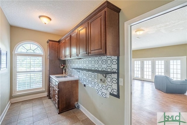 kitchen with light wood-type flooring, a textured ceiling, backsplash, and sink