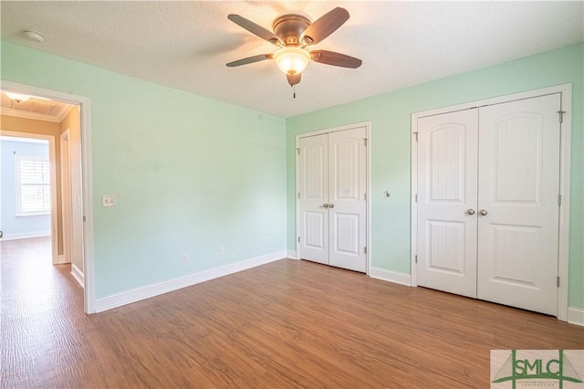 unfurnished bedroom featuring light wood-type flooring, two closets, ceiling fan, and ornamental molding