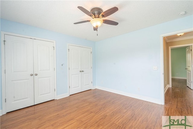 unfurnished bedroom with ceiling fan, two closets, crown molding, and light hardwood / wood-style flooring