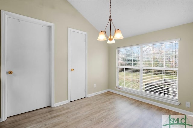 unfurnished dining area with light hardwood / wood-style floors, vaulted ceiling, and an inviting chandelier