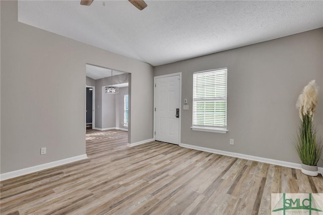 unfurnished room featuring ceiling fan with notable chandelier, a textured ceiling, and light wood-type flooring