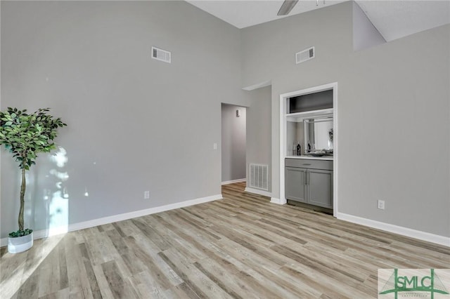 unfurnished living room featuring a towering ceiling, light hardwood / wood-style floors, and ceiling fan