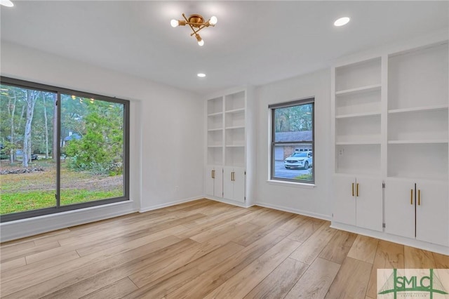 unfurnished living room with an inviting chandelier, a healthy amount of sunlight, and light wood-type flooring