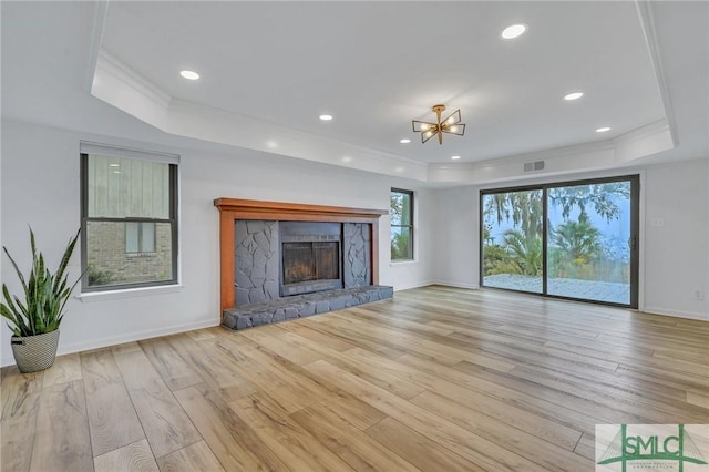 unfurnished living room with a raised ceiling, a stone fireplace, light hardwood / wood-style floors, and ornamental molding