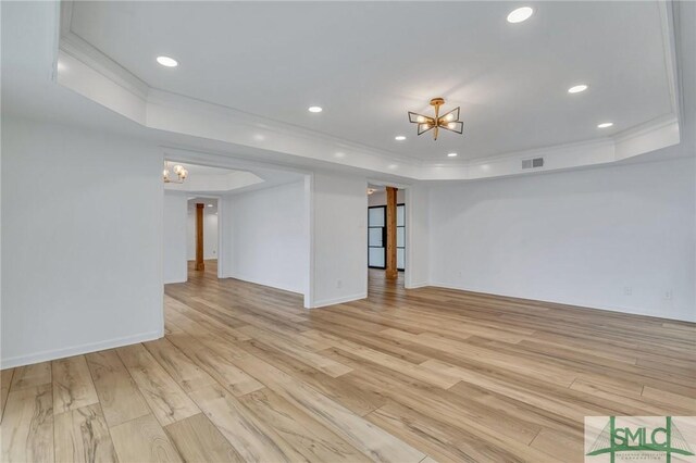 spare room with a tray ceiling, a chandelier, and light wood-type flooring