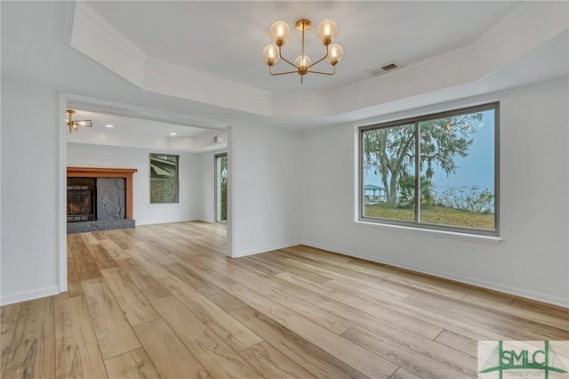 unfurnished living room with an inviting chandelier, a stone fireplace, light hardwood / wood-style flooring, crown molding, and a tray ceiling