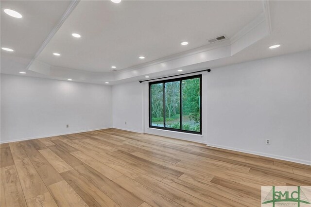 empty room featuring light hardwood / wood-style floors, a raised ceiling, and ornamental molding