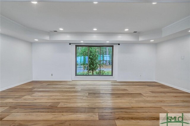 empty room featuring light hardwood / wood-style floors, a tray ceiling, and ornamental molding