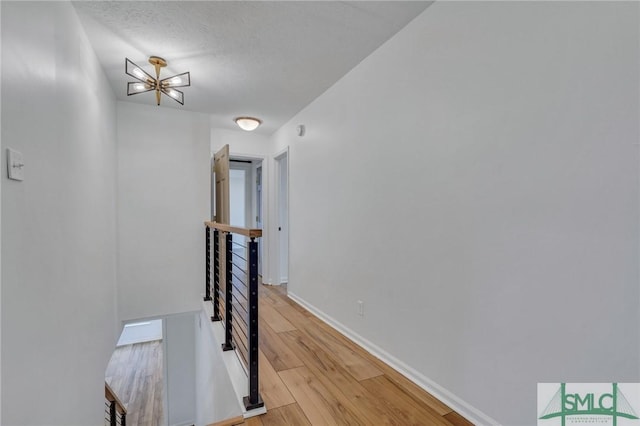 hall featuring light hardwood / wood-style floors, a textured ceiling, and an inviting chandelier