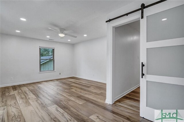 empty room with a barn door, ceiling fan, and light wood-type flooring