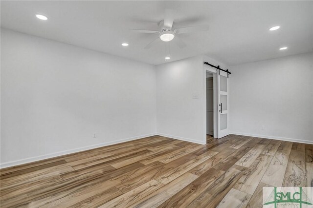 unfurnished room with a barn door, ceiling fan, and light hardwood / wood-style flooring