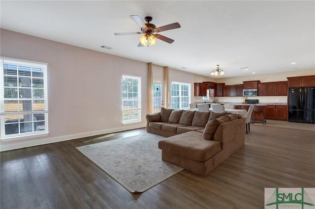 living room featuring ceiling fan with notable chandelier and dark wood-type flooring