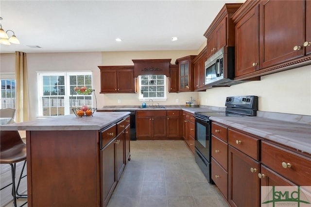 kitchen featuring a breakfast bar, black appliances, sink, hanging light fixtures, and a kitchen island