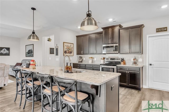 kitchen featuring dark brown cabinetry, stainless steel appliances, pendant lighting, a kitchen bar, and a kitchen island with sink