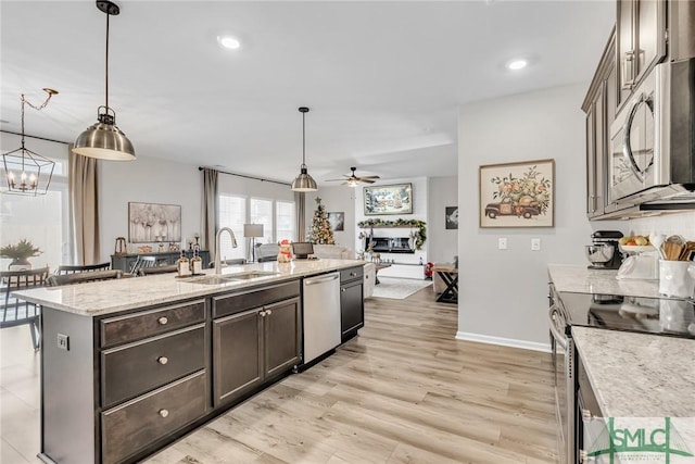 kitchen featuring appliances with stainless steel finishes, light wood-type flooring, a kitchen island with sink, sink, and hanging light fixtures