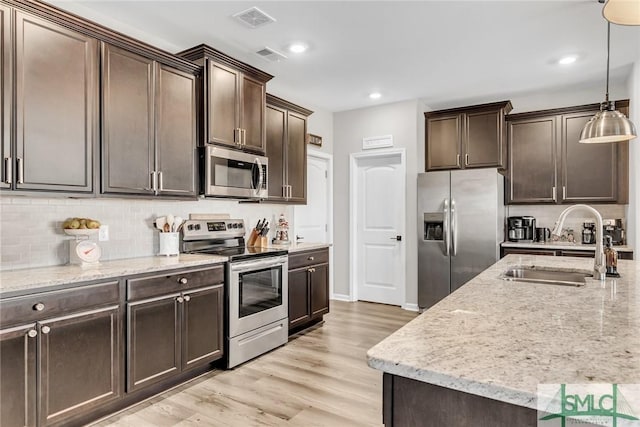 kitchen with appliances with stainless steel finishes, dark brown cabinetry, sink, decorative light fixtures, and light hardwood / wood-style floors