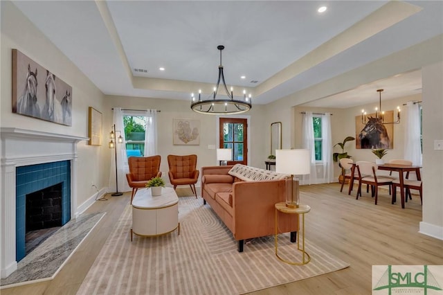 living room featuring a chandelier, light hardwood / wood-style floors, a raised ceiling, and a fireplace