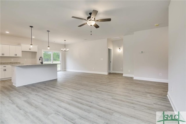 unfurnished living room with light wood-type flooring, ceiling fan with notable chandelier, and sink