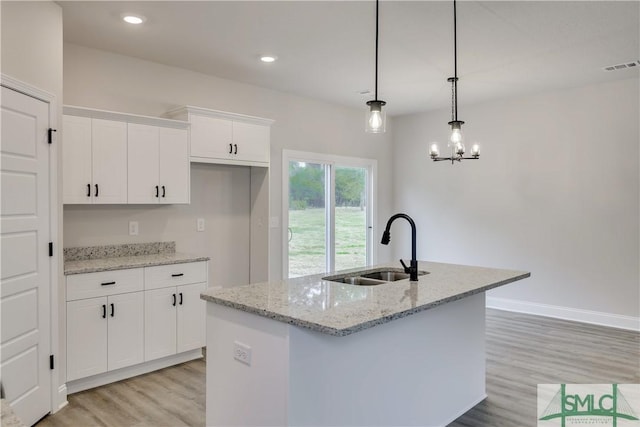 kitchen with light stone countertops, a kitchen island with sink, sink, pendant lighting, and white cabinetry