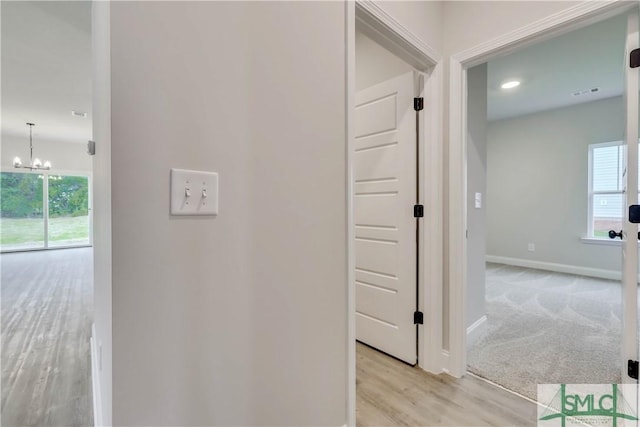 hall with light hardwood / wood-style flooring, a healthy amount of sunlight, and a notable chandelier