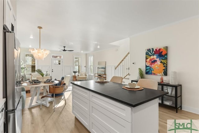 kitchen featuring stainless steel refrigerator, white cabinetry, pendant lighting, a kitchen island, and ceiling fan with notable chandelier