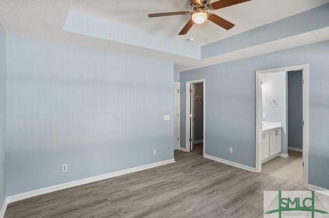 unfurnished bedroom with a walk in closet, light wood-type flooring, connected bathroom, and ceiling fan