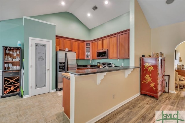 kitchen featuring kitchen peninsula, appliances with stainless steel finishes, dark stone counters, high vaulted ceiling, and a breakfast bar area