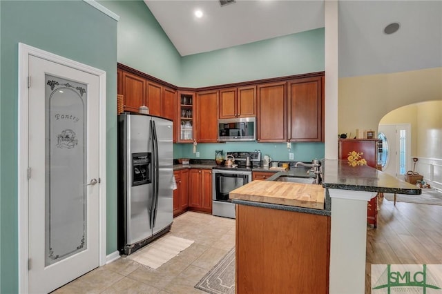 kitchen with kitchen peninsula, appliances with stainless steel finishes, vaulted ceiling, sink, and light tile patterned flooring