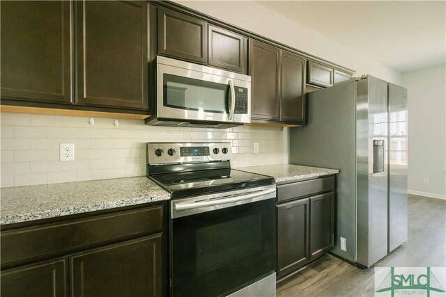 kitchen featuring dark brown cabinetry, light stone countertops, stainless steel appliances, and light wood-type flooring