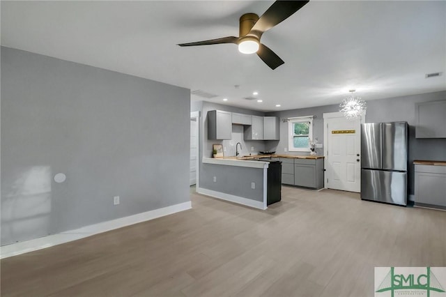 kitchen featuring sink, stainless steel fridge, gray cabinets, ceiling fan with notable chandelier, and light wood-type flooring