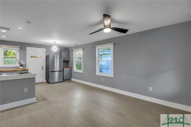 kitchen with stainless steel refrigerator, a healthy amount of sunlight, ceiling fan with notable chandelier, and light wood-type flooring