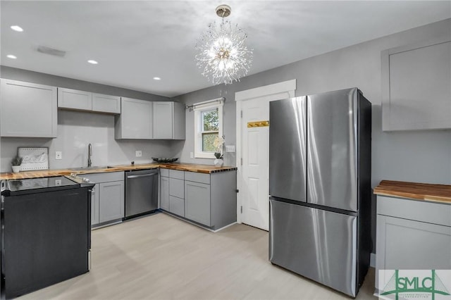 kitchen featuring gray cabinetry, appliances with stainless steel finishes, a notable chandelier, light hardwood / wood-style floors, and butcher block counters