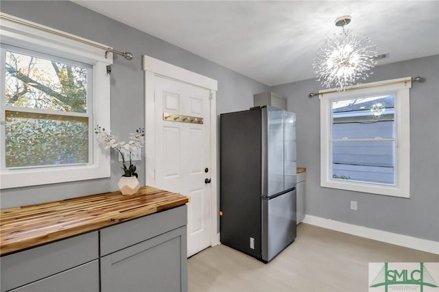 kitchen featuring gray cabinetry, decorative light fixtures, a notable chandelier, butcher block counters, and stainless steel refrigerator