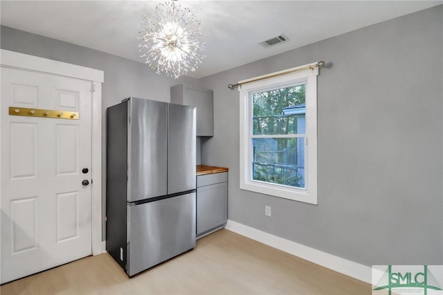 kitchen with stainless steel fridge, light hardwood / wood-style floors, and a notable chandelier