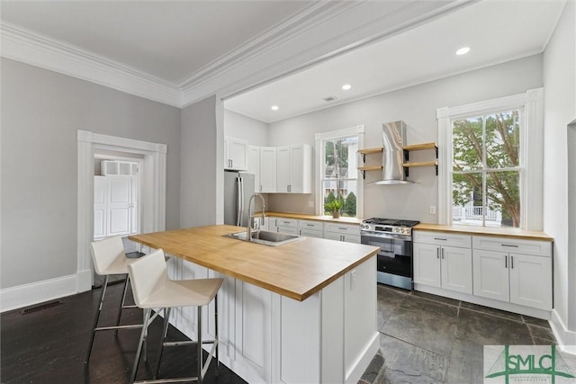 kitchen with stainless steel appliances, wood counters, a sink, wall chimney range hood, and white cabinets