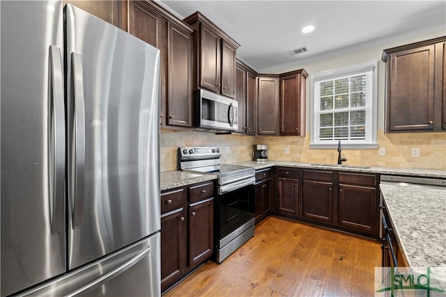 kitchen featuring light stone countertops, sink, stainless steel appliances, crown molding, and light wood-type flooring