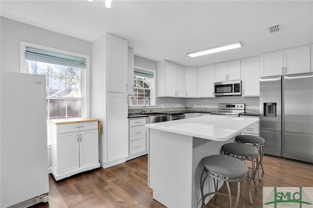 kitchen with dark hardwood / wood-style flooring, stainless steel appliances, sink, white cabinetry, and a kitchen island