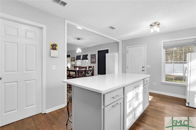 kitchen with dark hardwood / wood-style flooring, a center island, white fridge, and a kitchen breakfast bar