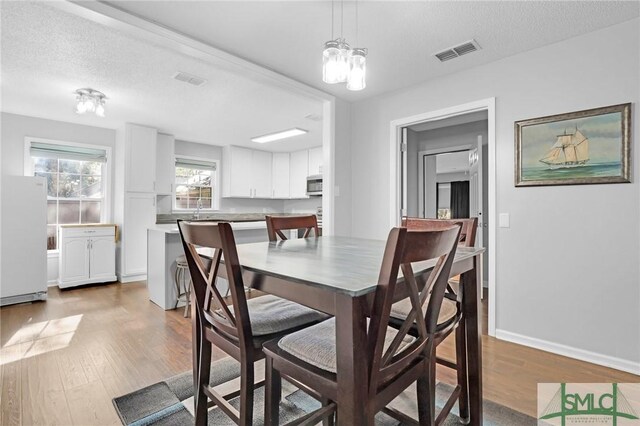 dining room with a textured ceiling, light wood-type flooring, an inviting chandelier, and sink