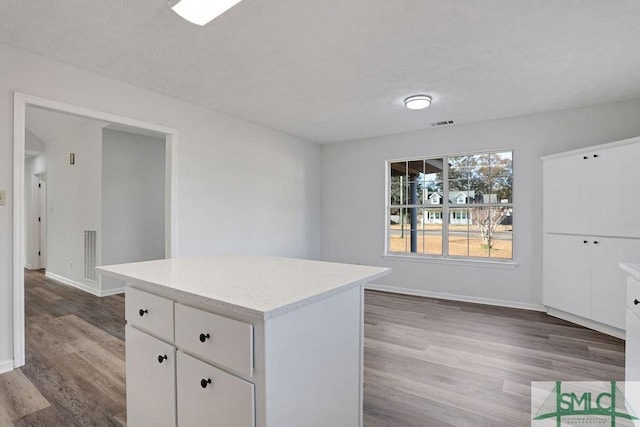 kitchen with white cabinets, a textured ceiling, hardwood / wood-style flooring, and a kitchen island