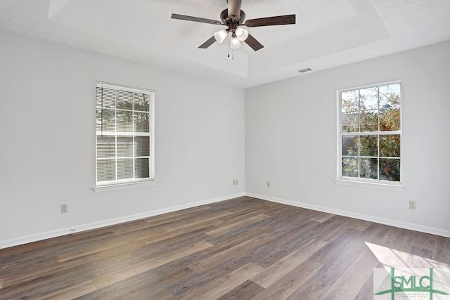 empty room with a tray ceiling, ceiling fan, and hardwood / wood-style flooring